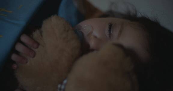 小女孩在卧室里吸着奶嘴抱着小熊睡觉