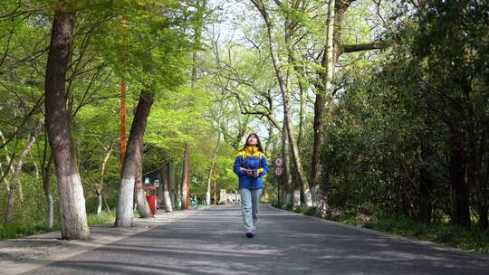 阳光明媚的春天年轻女孩拿着相机在路上拍照