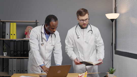 两名医生在诊所站着用笔记本电脑说话
