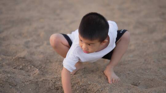男孩在水边的沙滩上用塑料锹和水桶玩沙子