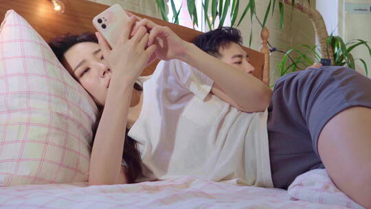 青年情侣坐在床上各自玩手机