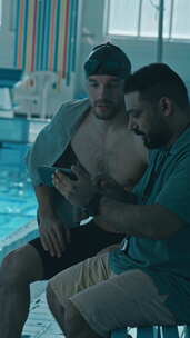 男游泳运动员与教练用智能手机探讨泳池中的