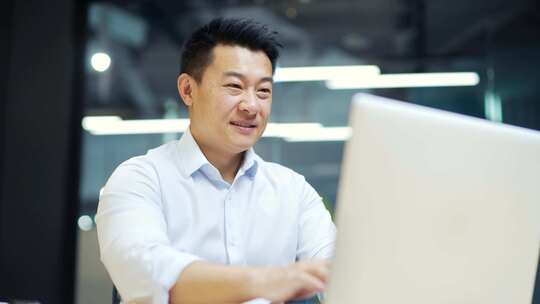 快乐的亚洲男性员工在现代办公室的笔记本电