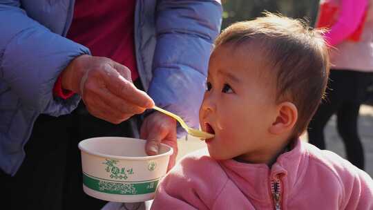 老人用勺子给小孩喂食的温馨画面