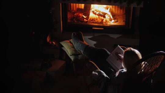 年轻女人坐在壁炉旁看书