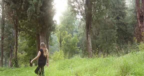 穿黑色连衣裙的女人在树林里穿过草地