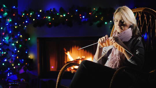 女人在圣诞装饰的壁炉旁织衣服