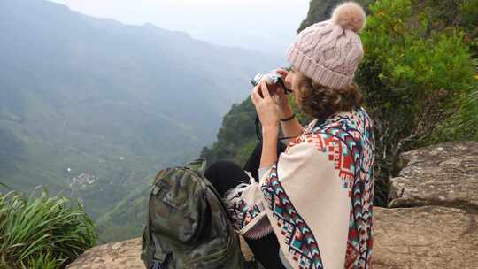 背着背包的年轻女子旅行者在山顶上用相机拍