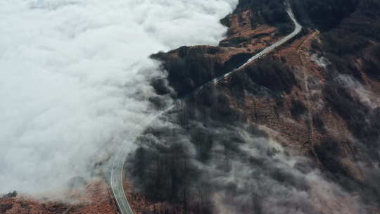 一条蜿蜒的道路穿过雾蒙蒙的山景，云层盘旋