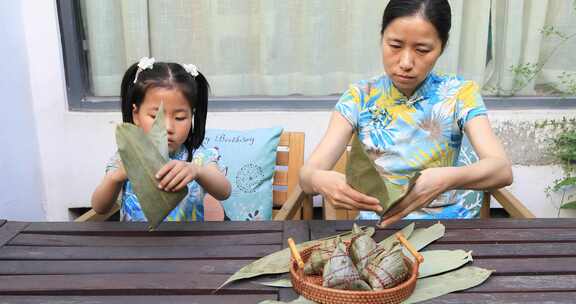 端午节 妈妈在院子里教女儿用粽叶包粽子