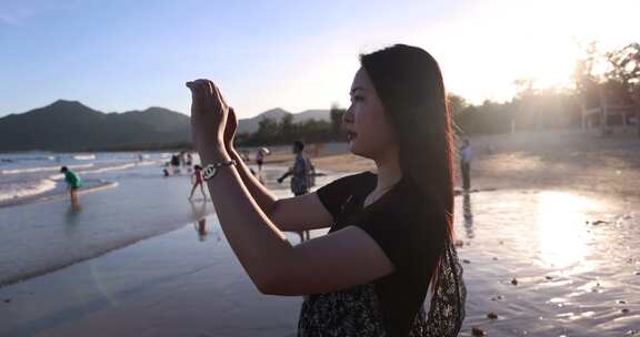 美女用手机在海边拍照