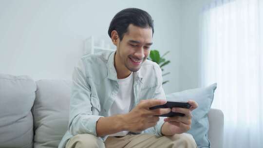 亚洲男子在家玩手机游戏视频素材模板下载