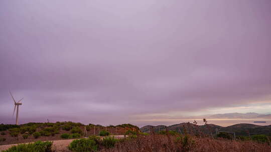 风力涡轮机在黎明时分在紫色天空下的丘陵地