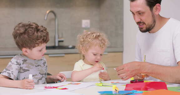 小女孩和小男孩正在用彩纸和胶水和他们的父亲做应用