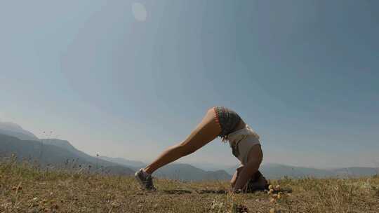 阳光明媚的一天，年轻女孩试图在山上做瑜伽倒立
