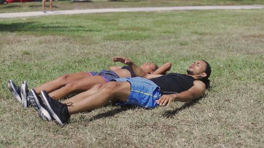 夫妇躺在草地上做热身运动视频素材模板下载