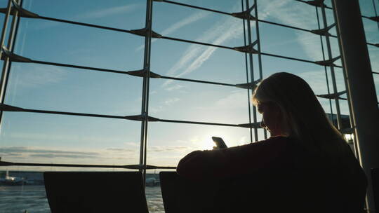 女人在机场航站楼窗户前使用手机的剪影