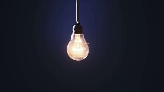 电线上的经典灯泡在蓝色背景上闪烁并点亮