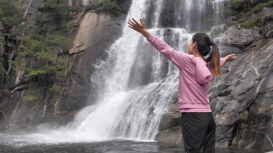 中国人女性在瀑布下张开双臂拥抱自然