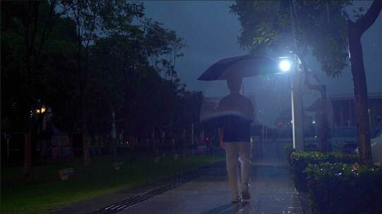 男生撑伞走在雨中行走