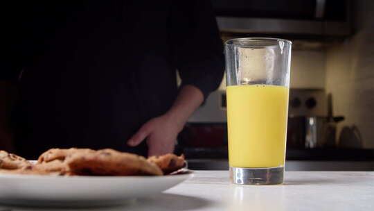 一名身穿黑色毛衣的男子将橙汁倒入家中厨房的玻璃杯中