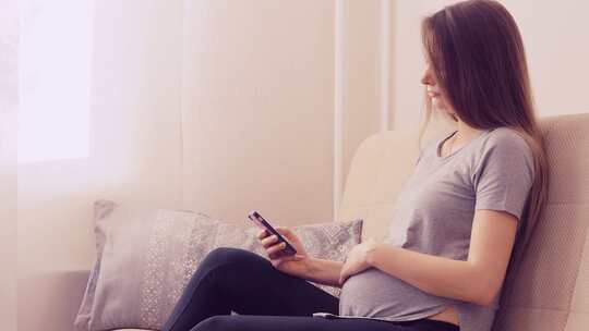 坐在沙发上的孕妇在使用手机视频素材模板下载