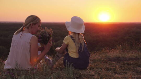 妈妈拿着野花和小女儿坐在山头欣赏日落