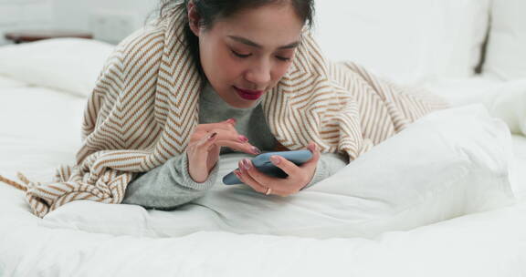 年轻亚洲女孩躺在床上玩手机发消息