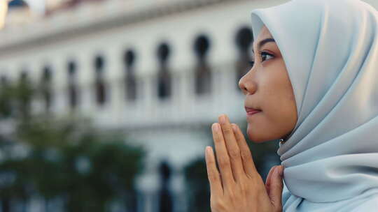 年轻的穆斯林女孩在外面牵手一起祈祷戴头巾