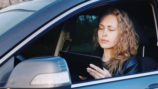 女人坐在汽车主驾驶上使用平板电脑视频素材模板下载
