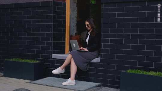 一名年轻女子坐在窗台上使用笔记本电脑