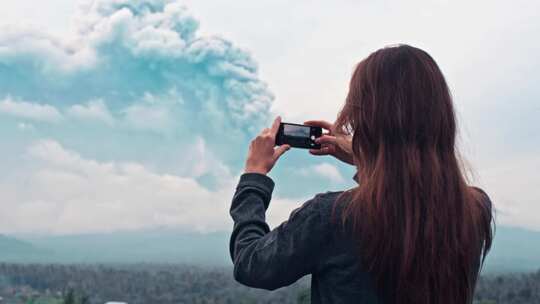 女人用手机拍火山爆发的照片