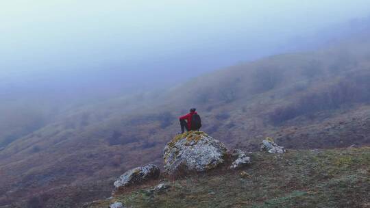 一个旅行者坐在山顶石头上
