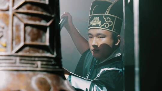 头戴乌纱帽的男子敲钟的画面