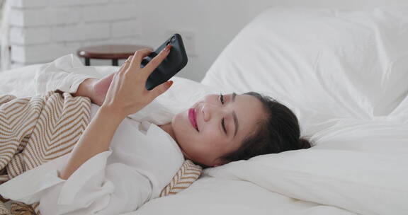 女青年家躺在床上用手机视频电话