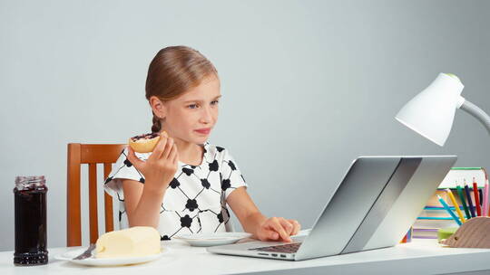 女孩笑着吃果酱黄油面包坐在笔记本电脑前