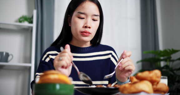 年轻的亚洲女人在家里的餐桌上享受美食。