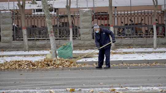 冬天下雪天环卫工人在路边清扫落叶