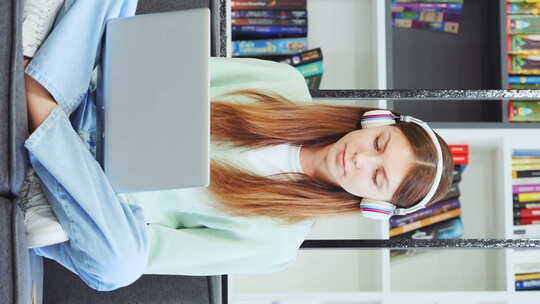 垂直屏幕：戴着耳机在笔记本电脑上唱歌的女青少年