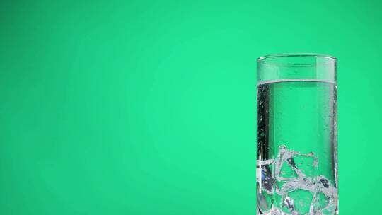 装满冰块的冰水的玻璃在绿色背景上旋转。