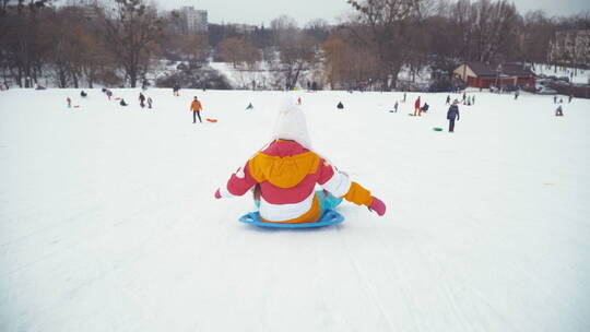 女孩坐在雪盘上滑下雪山