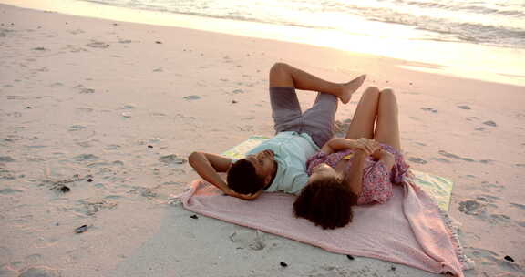 日落时分，出生夫妇在沙滩巾上放松，有复印