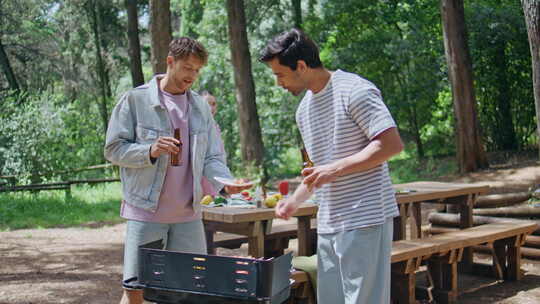 两个男人在夏季森林烧烤时拿着啤酒烧烤特写