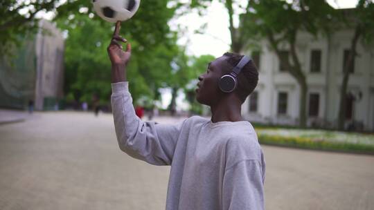 男人戴着耳机在街头用手指旋转足球