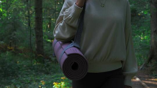 女人拿瑜伽垫在树林里行走的特写视频素材模板下载