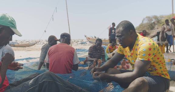 渔民在海滩坐着割渔网