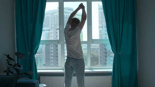 清晨，男人锻炼的剪影，在家靠窗伸展身体。