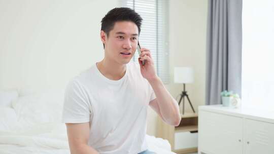 亚洲帅哥早上在家床上打手机通话。
