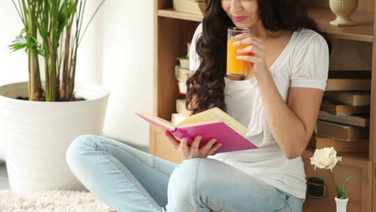 女孩坐在地板上看书喝果汁