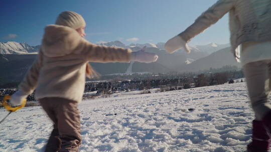母女手牵手拉着雪橇在雪山下奔跑